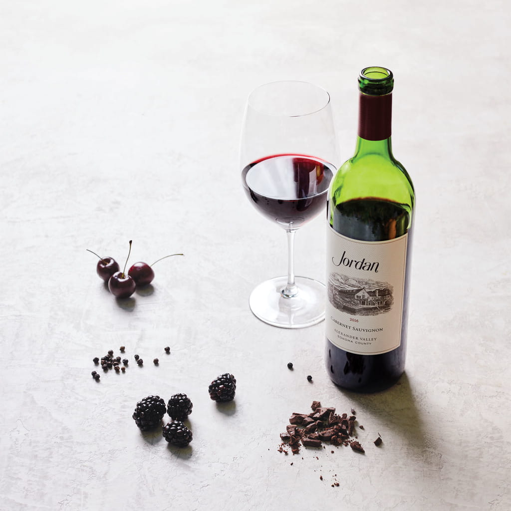 Bottle of 2016 Jordan Cabernet Sauvignon on a table with typical aromatics: cherries, blackberries, peppercorns and chocolate