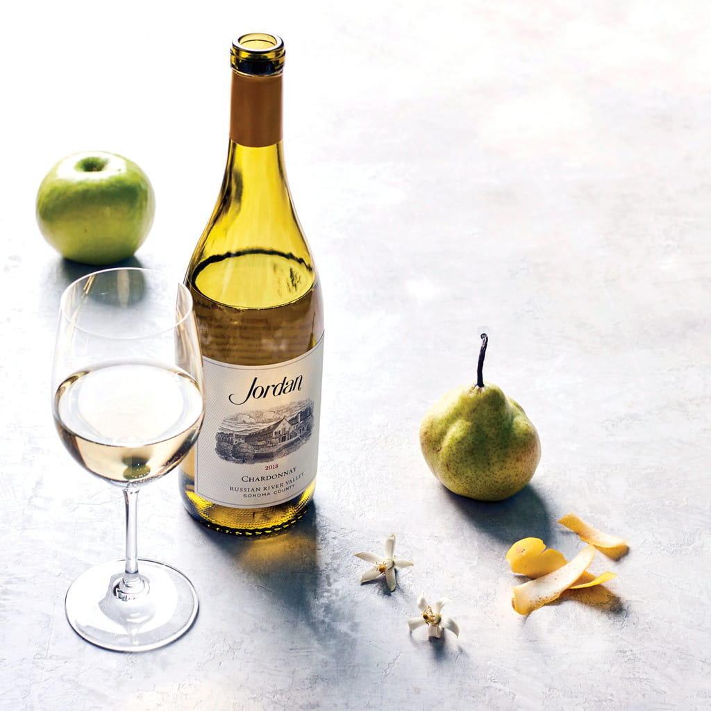 Bottle of 2018 Jordan Chardonnay on a table with typical aromatics: green apple, pear, lemon peel and citrus blossom