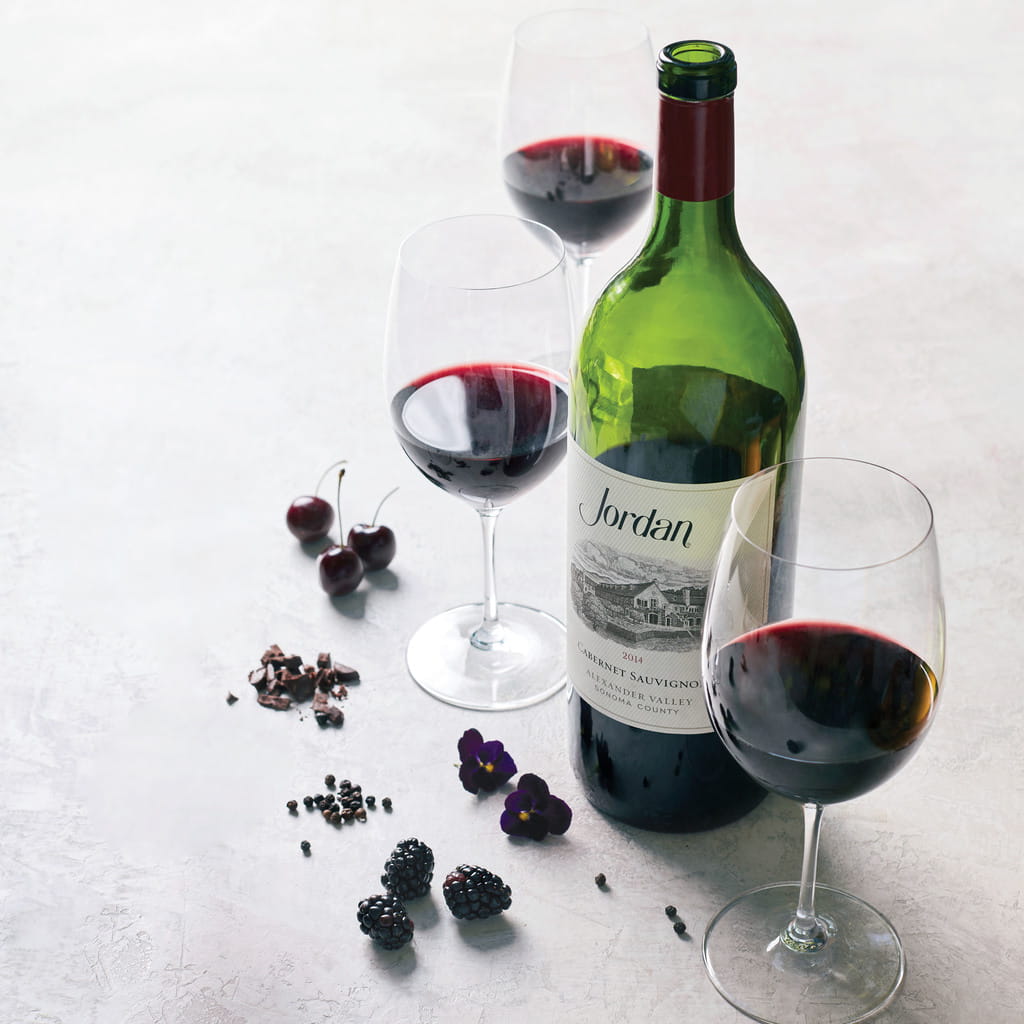 Magnum bottle of 2014 Jordan Cabernet Sauvignon on a table with typical aromatics: black cherries, chocolate, peppercorns, blackberries and violets